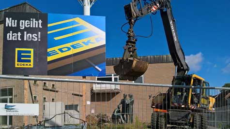 Post, Abbrucharbeiten hinter Bauzaun und Bauschild, Bagger über Goedtke-Skulptur